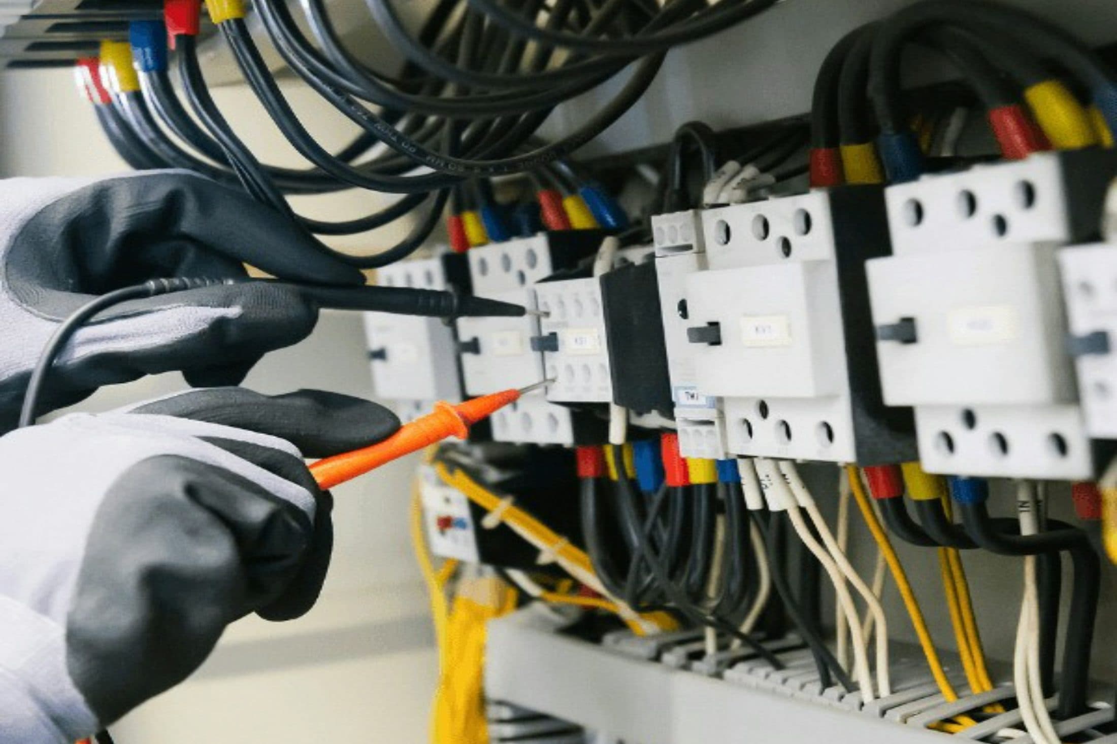 Les mains gantées d'un électricien qui testent au multimètre les bornes d'une armoire électrique câblée