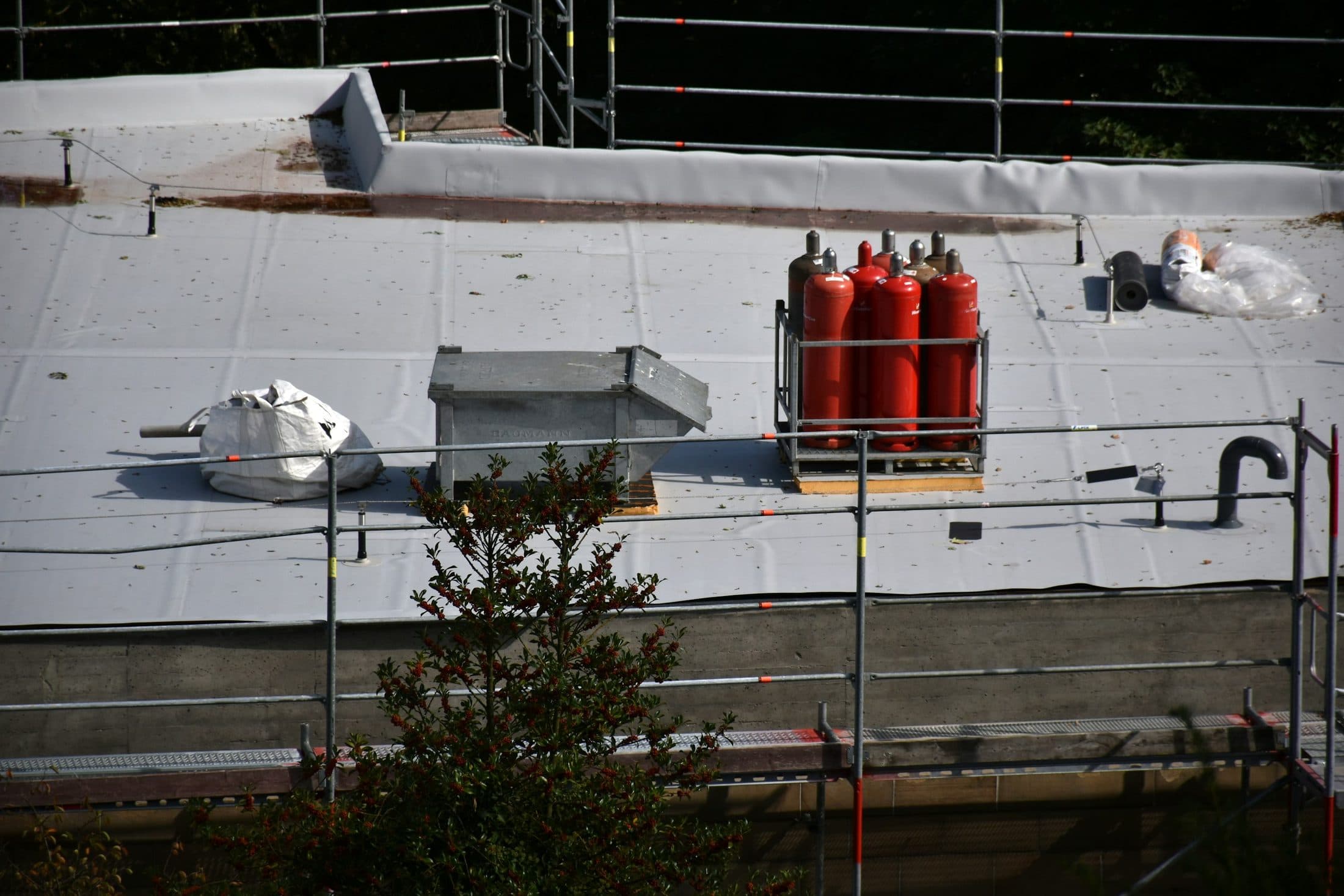 Une toiture-terrasse en cours d'étanchéité : membrane déroulée sur toute la surface, bouteilles de gaz du chalumeau, échafaudage en pourtour