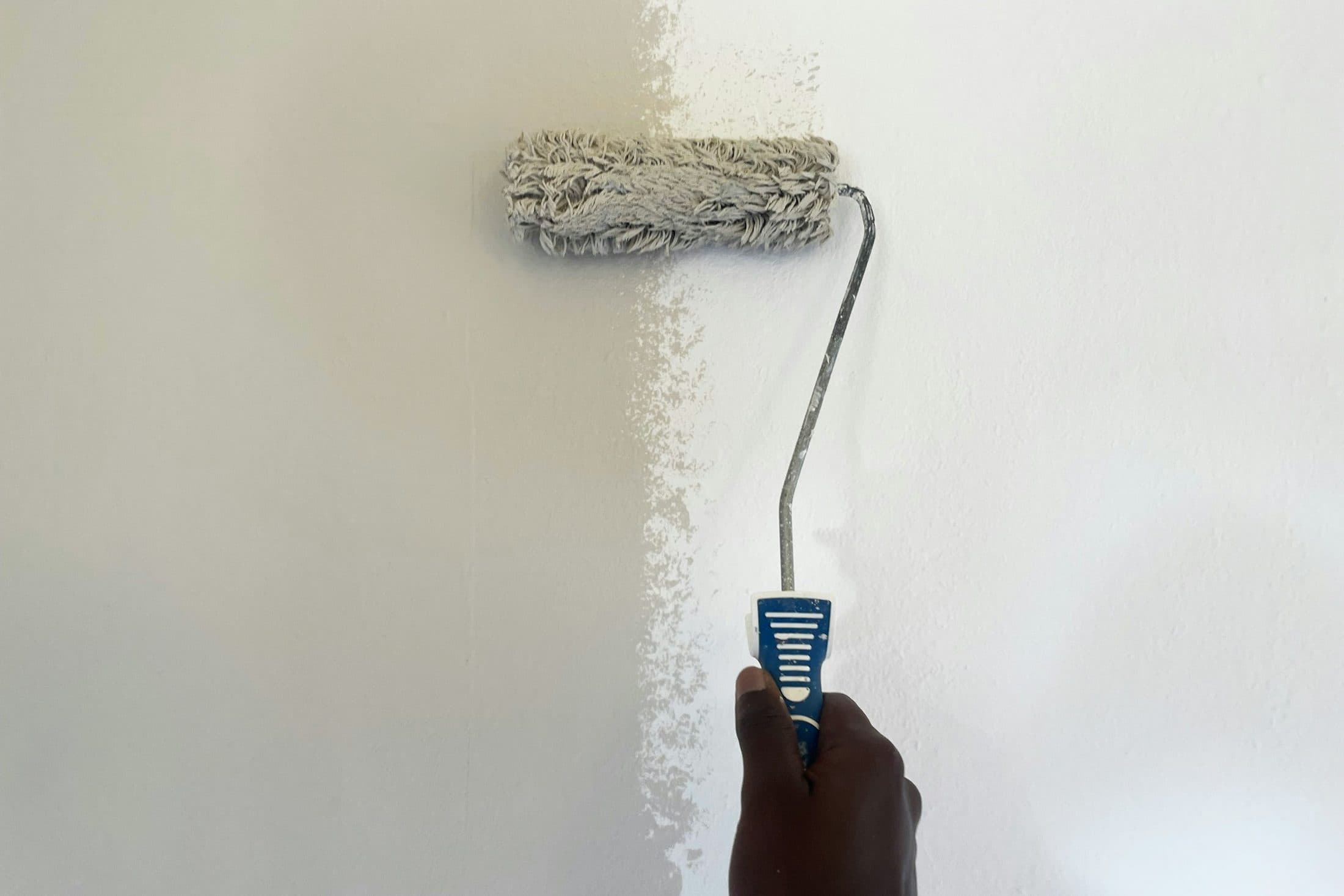 Une main qui passe un rouleau de peinture blanche sur un mur, la partie fraîchement peinte visible