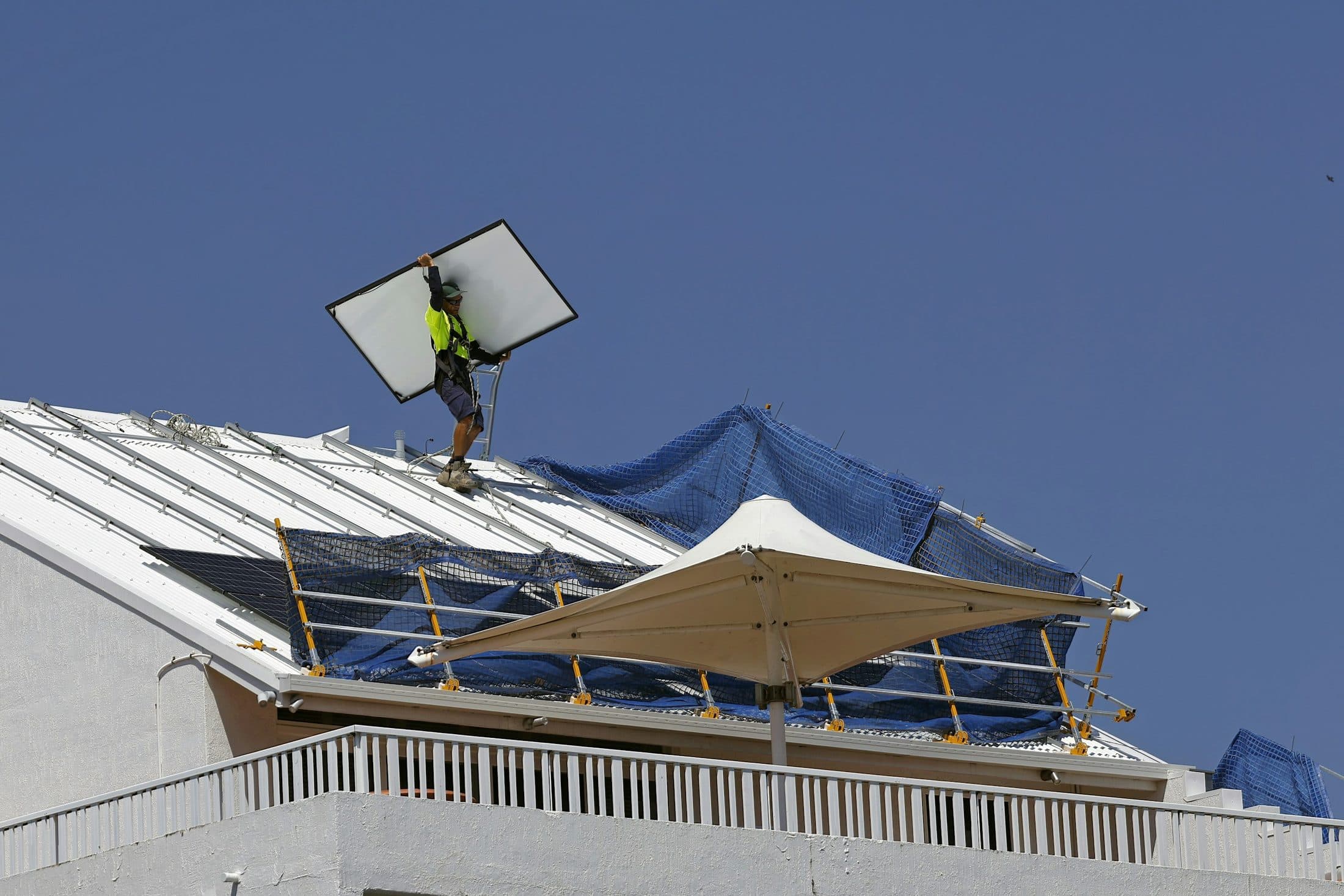 Un ouvrier qui porte un panneau solaire sur la toiture d'un bâtiment, sous un ciel bleu