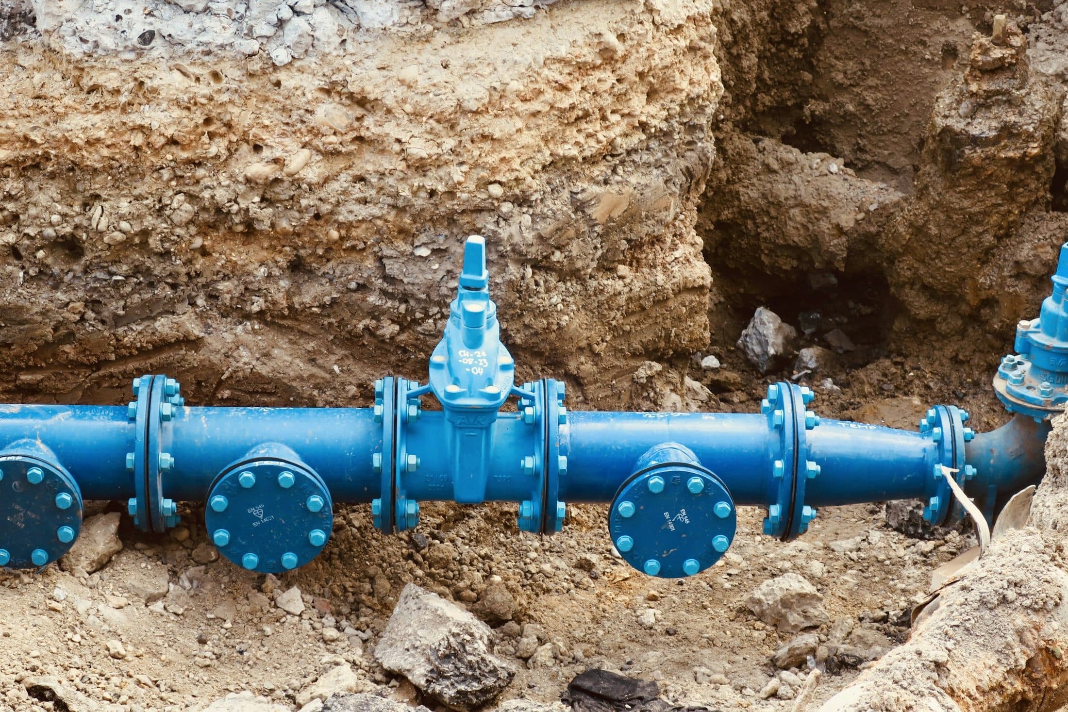 Une canalisation d'eau en fonte bleue avec ses vannes, posée au fond d'une tranchée ouverte