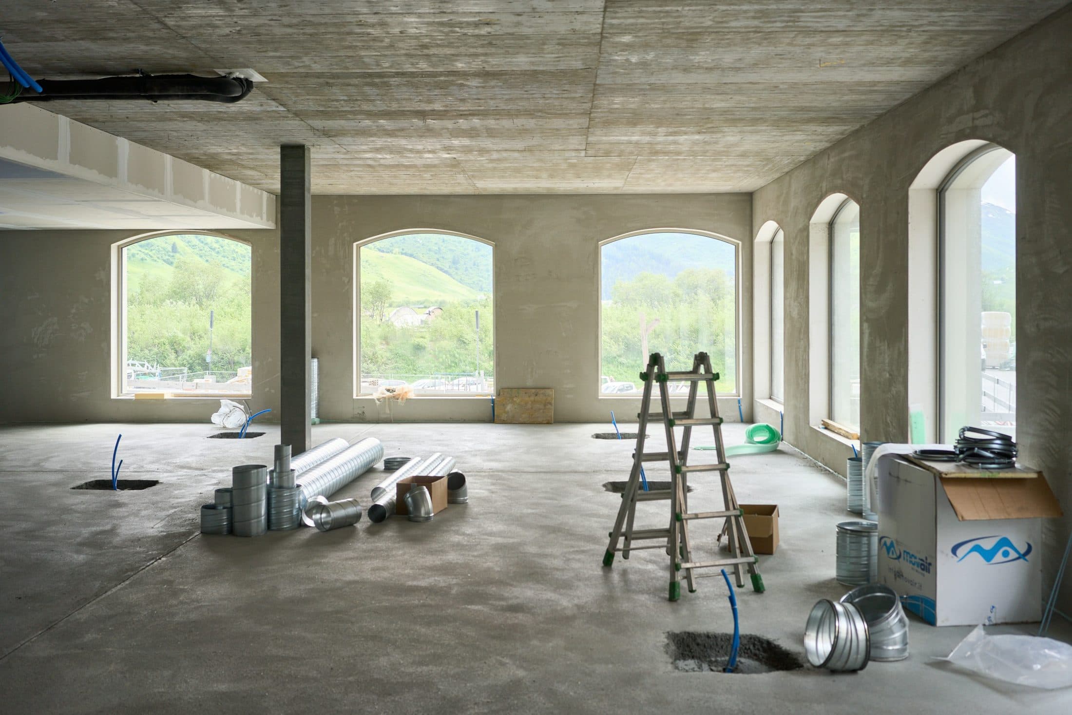 Un grand plateau en cours de second œuvre : plafond béton brut, escabeau, gaines de ventilation et matériaux au sol